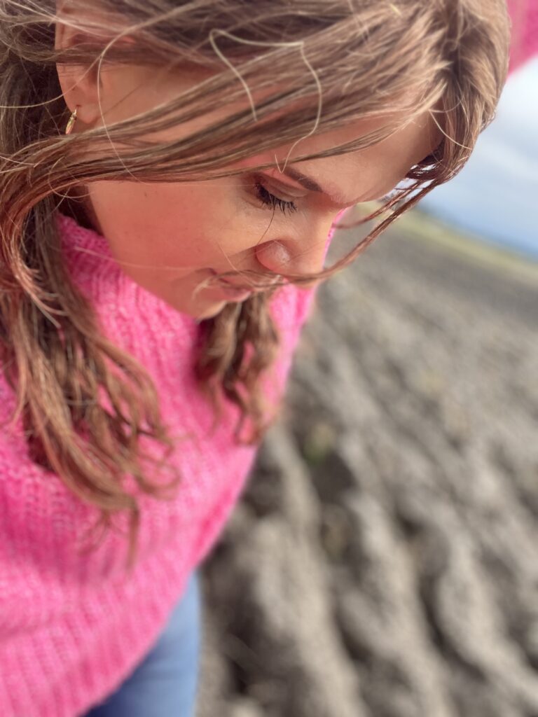 henkilö kävelee suomailessa maisemassa pinkki villapaita päällä ja hymyilee